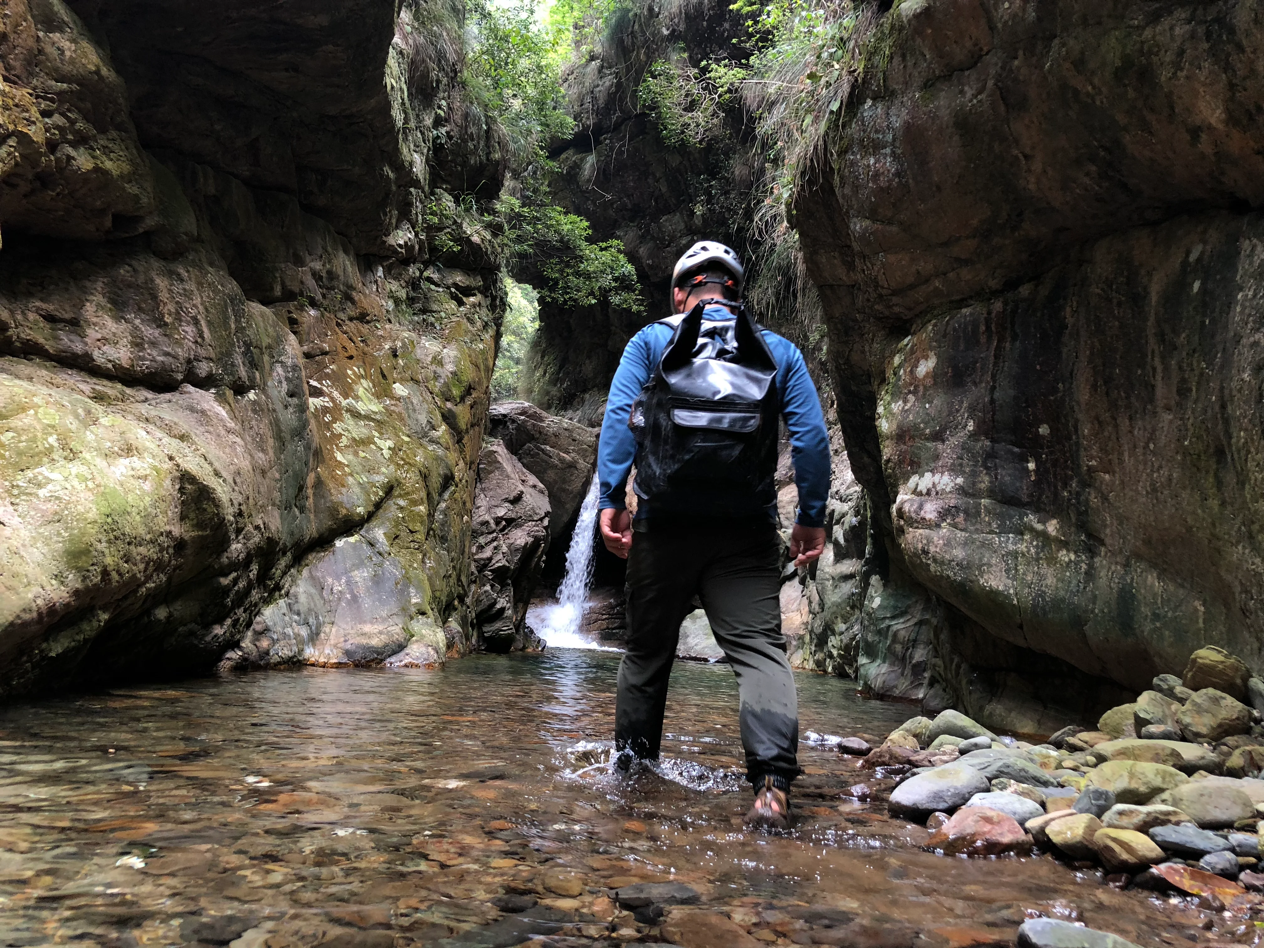 Guide in orange life jacket and red helmet walking along a rocky canyon stream in Guangxi, China