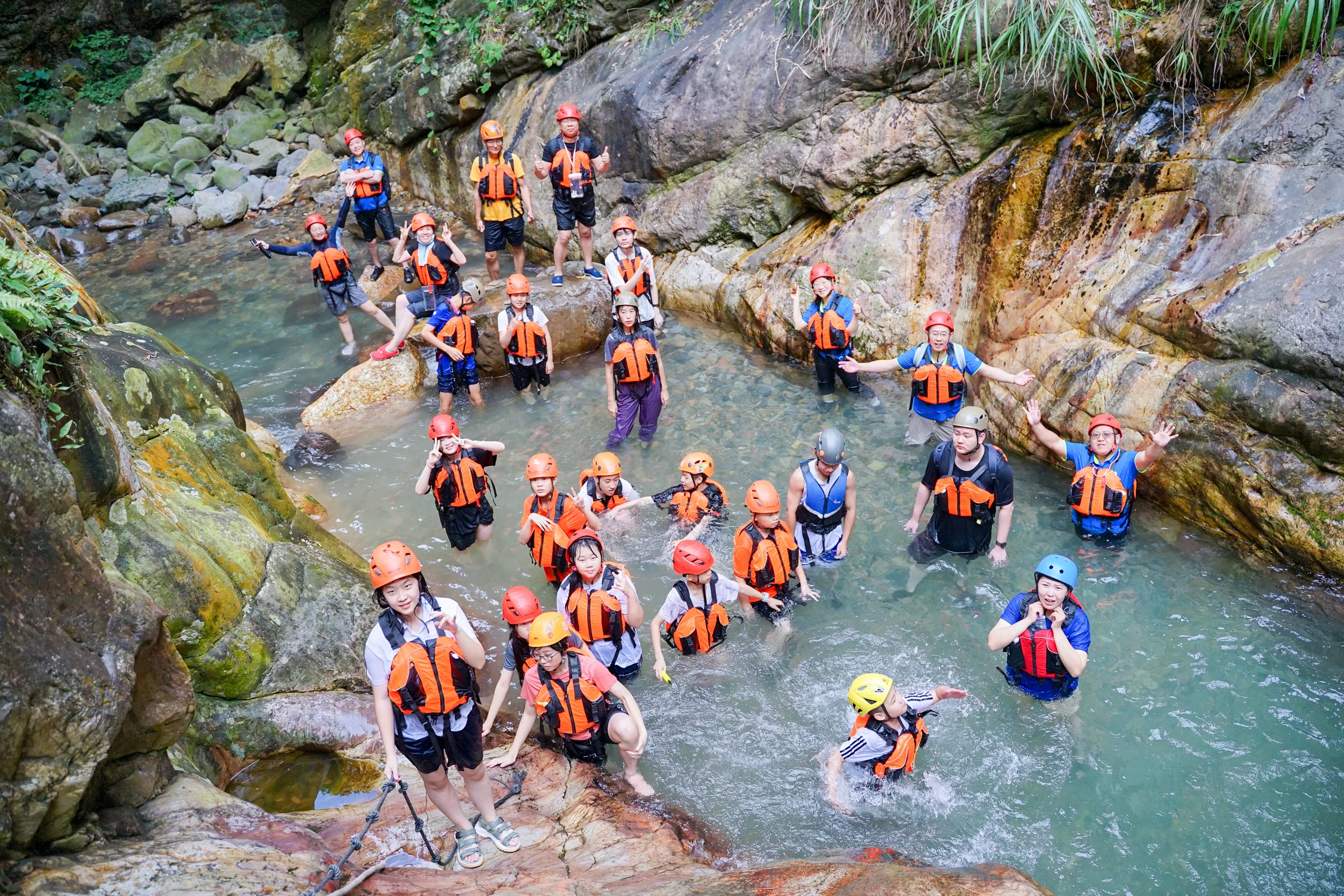 Adults and children in life jackets and helmets playing with water guns in a rocky mountain stream, China