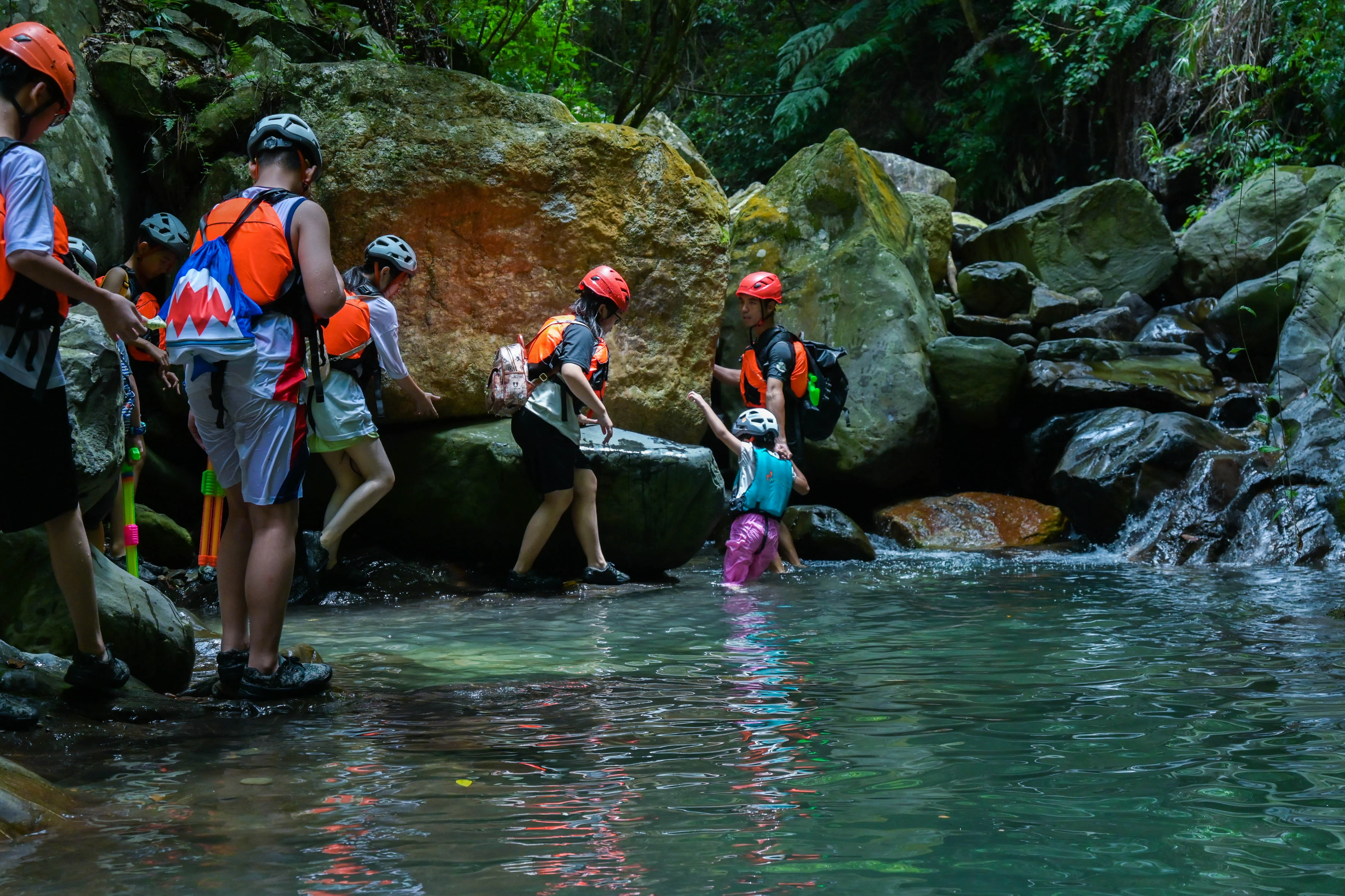 Three canyoneers chest-deep in a mountain stream with boulders and a small waterfall behind them, China