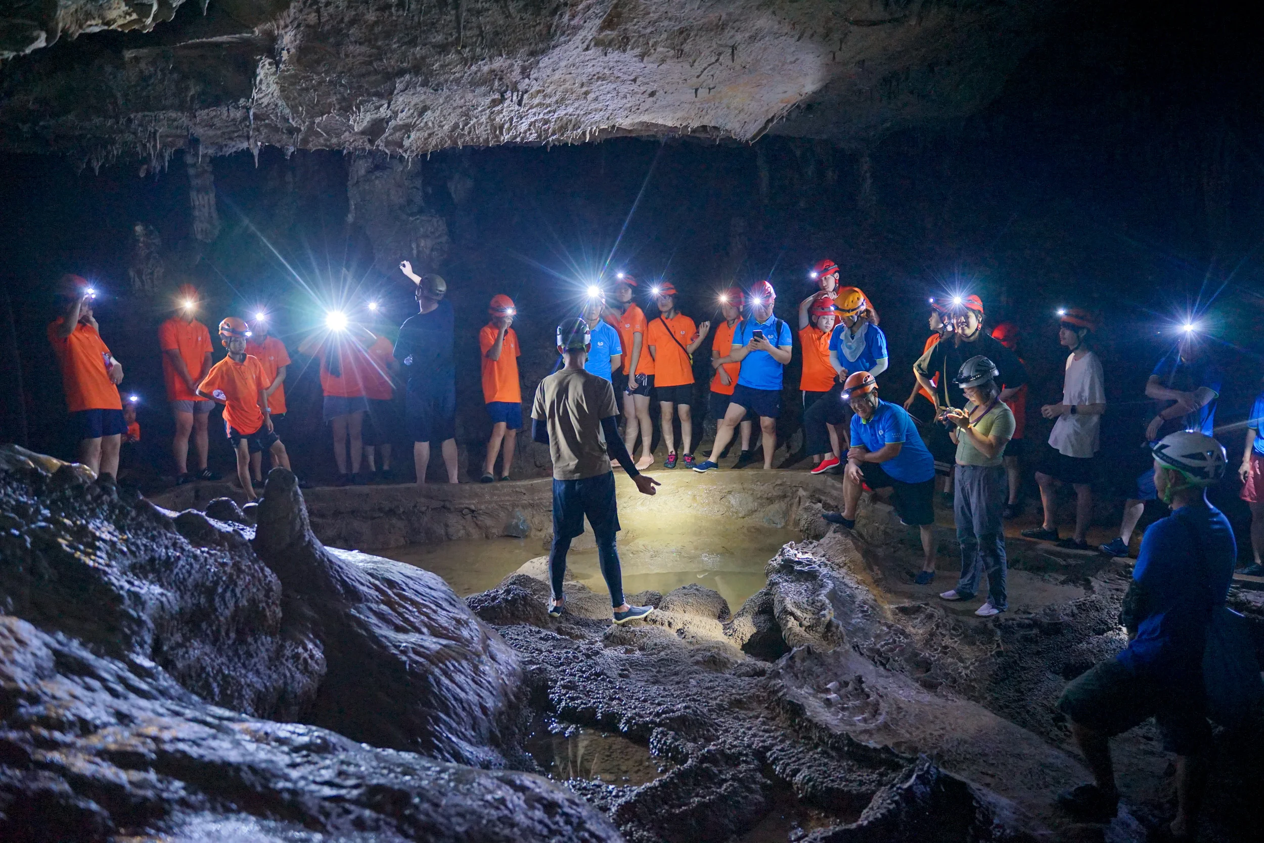 Guide explaining cave formations to a group of helmeted explorers inside a karst cave in Yangshuo