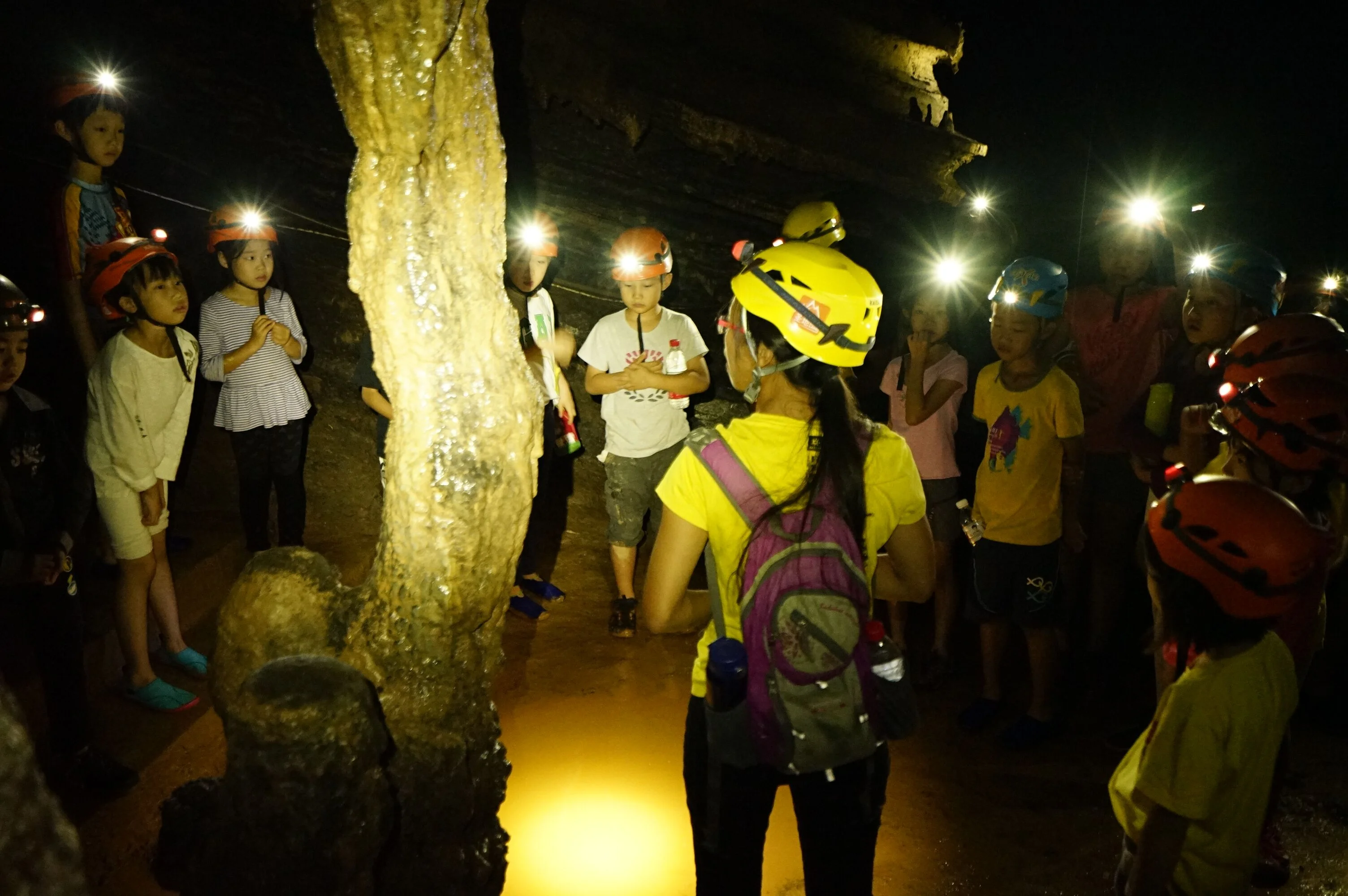 Group of explorers with headlamps observing dramatic stalactites in a Yangshuo karst cave