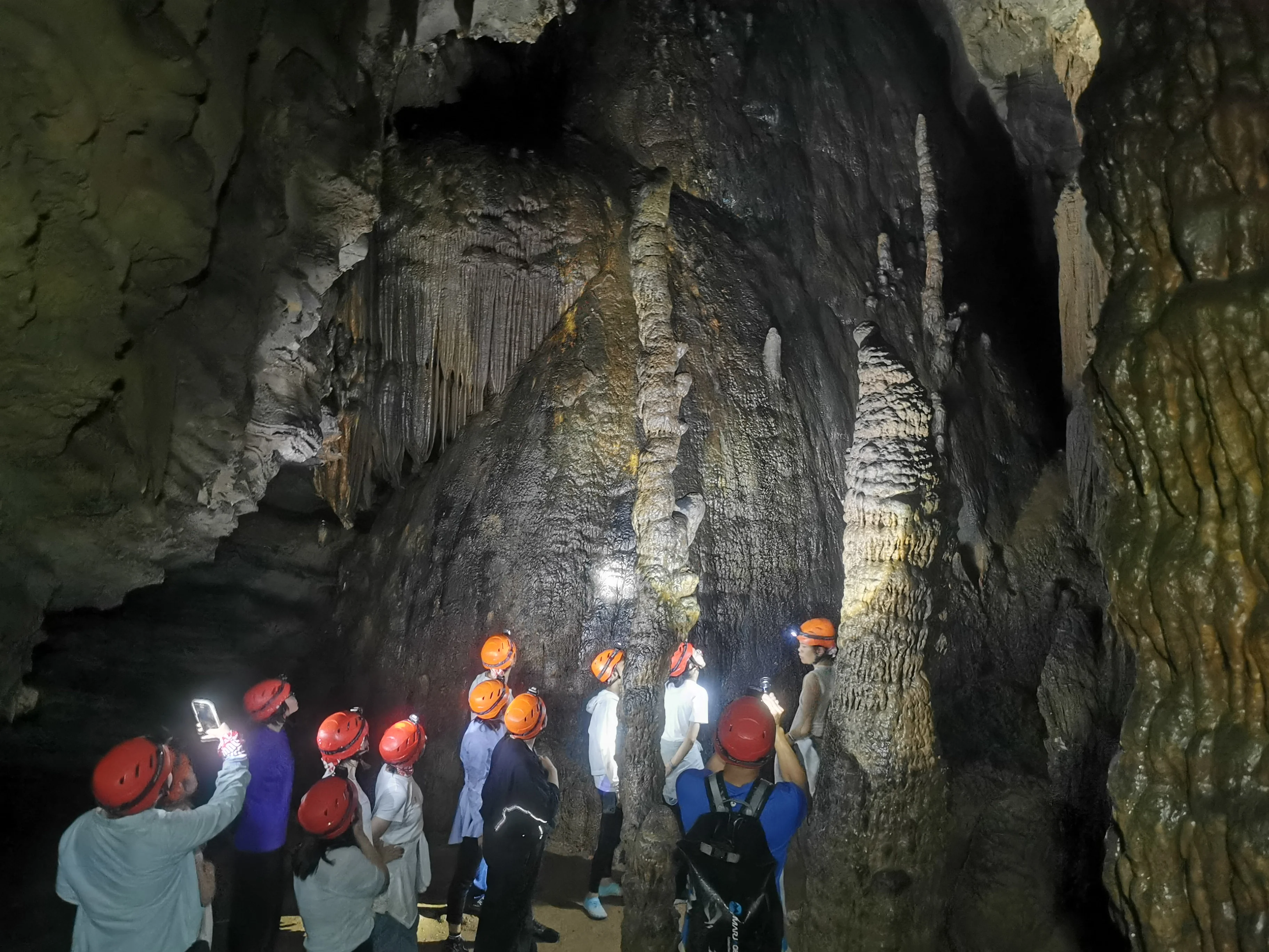 Explorers crouching through a low cave passage during a wild caving adventure in Yangshuo