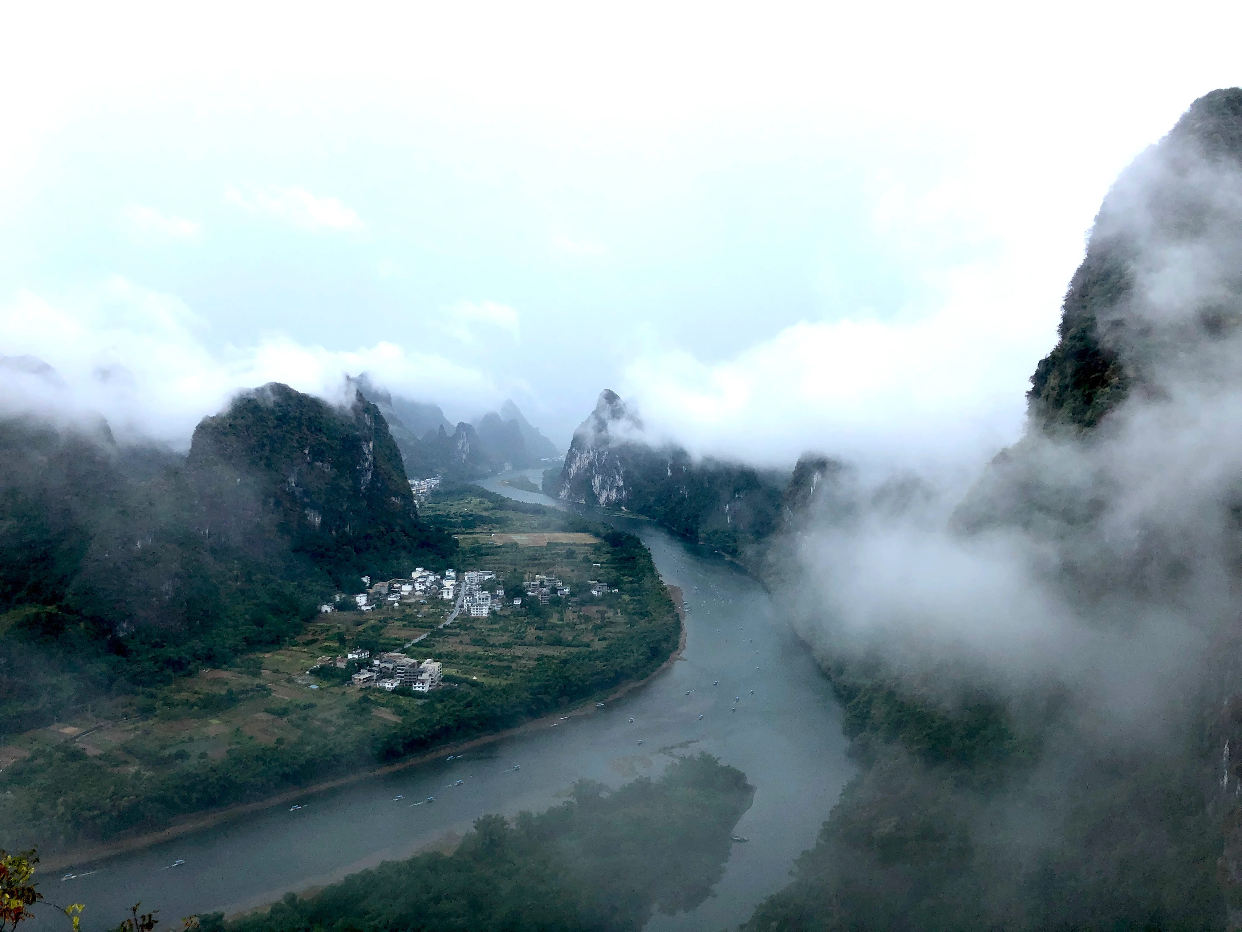 Group of hikers at a mountain viewpoint with a rainbow arcing over the terraced valley near Yangshuo