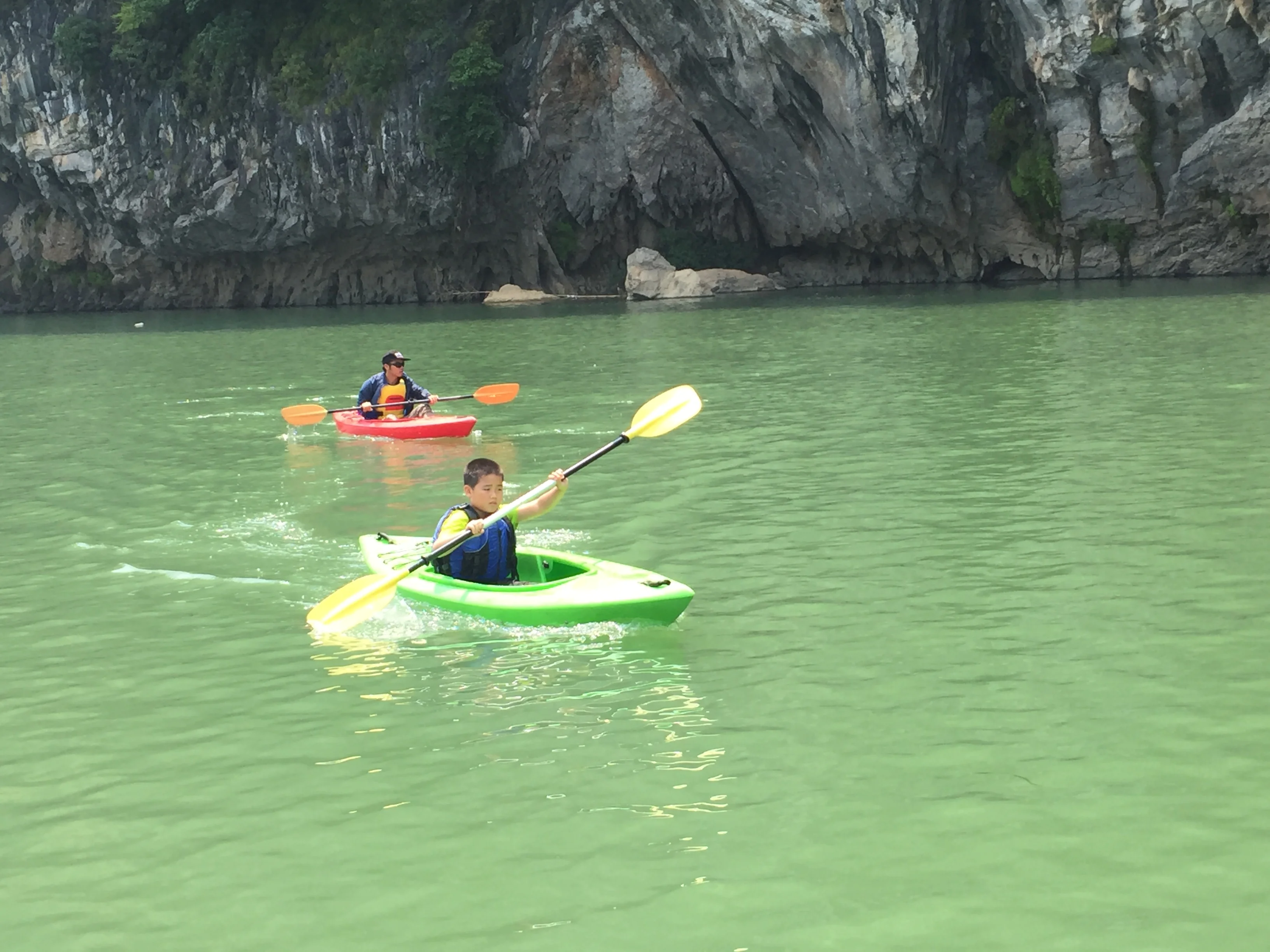 Family group with children kayaking, green karst mountains and a bridge in the background, Yangshuo