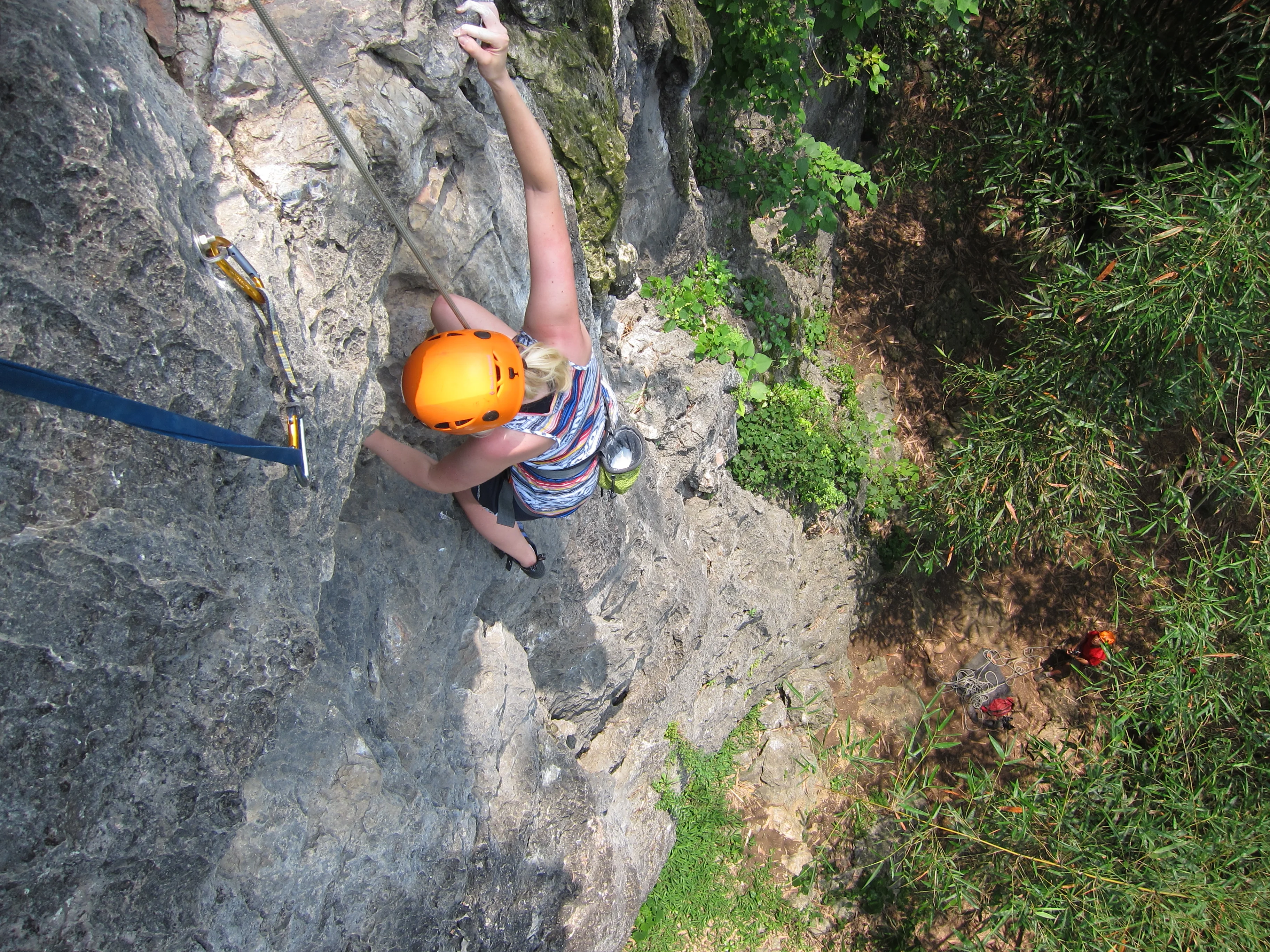 Young beginner climbing a karst rock face in Yangshuo with safety harness and helmet