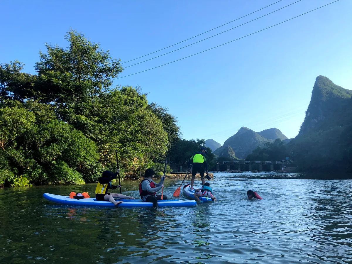 Family group on paddleboards, green karst mountains and a bridge in the background, Yangshuo