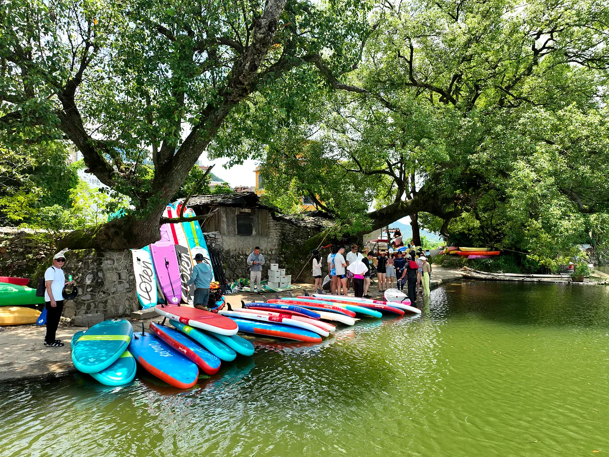Group in life jackets paddleboarding on the calm Yulong River with lush karst mountains reflected in the water, Yangshuo