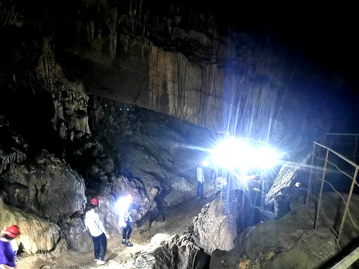 Group of visitors with helmets and headlamps walking along a cave pathway with stalactites, Guangxi China