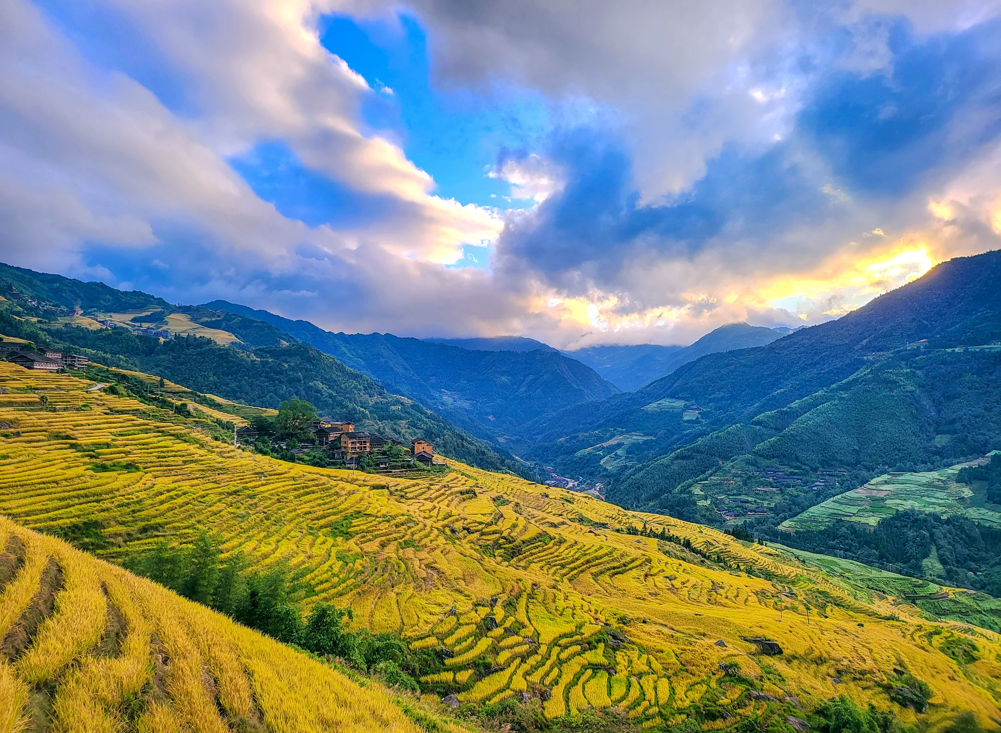 Traditional wooden village nestled among layered green mountains with morning mist, Guangxi China