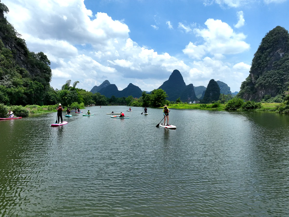 Aerial view of group paddleboarding on a winding river surrounded by karst peaks and farmland, China