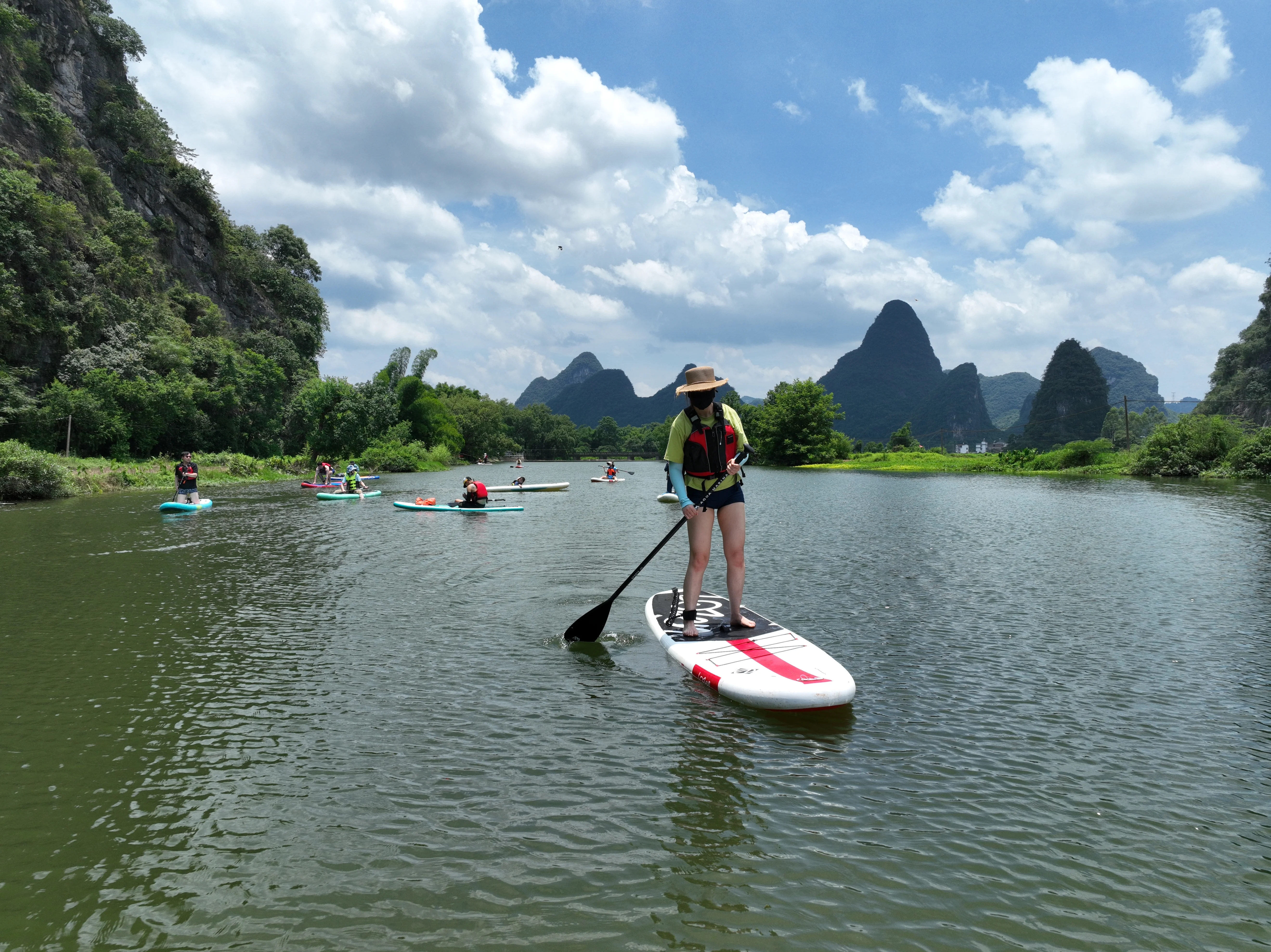 Aerial drone shot of paddleboarders in life jackets on a calm river with lush karst mountains, China